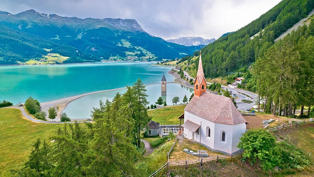 il borgo italiano dove le campane suonano sott’acqua: la torre emerge da un lago alpino
