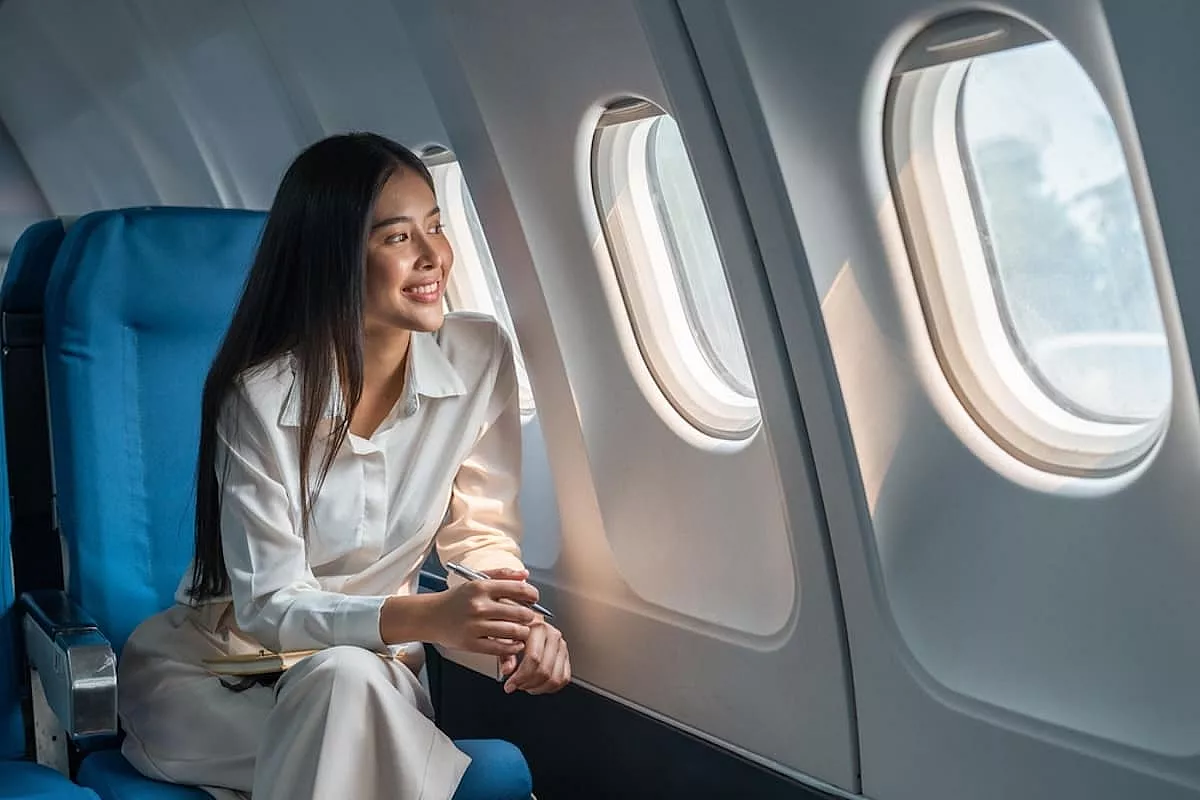 Donna sorridente che guarda fuori dal finestrino di un areoplano, viaggia per festeggiare la giornata della donna